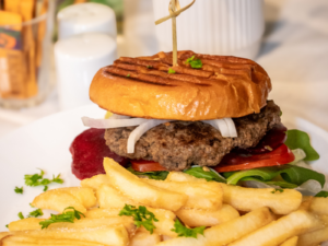 Grilled beef burger with lettuce, tomato, beetroot and onion on a toasted bun, served with golden hot chips on a white plate at STEPS Café on George.