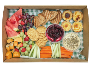 Freshly prepared morning tea catering box featuring seasonal fruit, crackers, vegetable sticks, dips, toasted banana bread and Portuguese tarts.